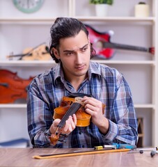 Young handsome repairman repairing violin