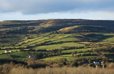 Landscape in rural County Sligo, Ireland featuring farm houses nestled amongst rolling hills of green field farmland pastures in Bricklieve Mountains