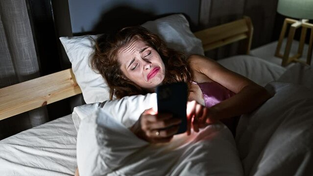A distressed woman in bed at night looking at her phone, depicting insomnia or bad news, in a dark bedroom setting.
