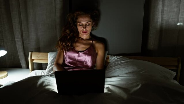 A young woman using a laptop in her bedroom at night, reflecting a modern lifestyle.