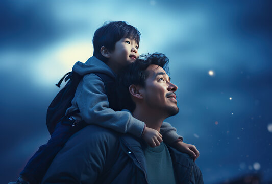 close up shot of father and son. Father giving son ride on back in park. Assian family and blue cloudy sky