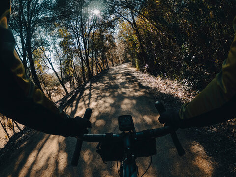 Riding a gravel bike with dorp handlebar between wood forest trees on a gravel path with sun flare shining through the branches