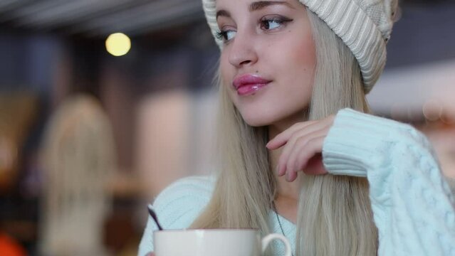 Blonde sits in cap looks around and on cup with spoon near