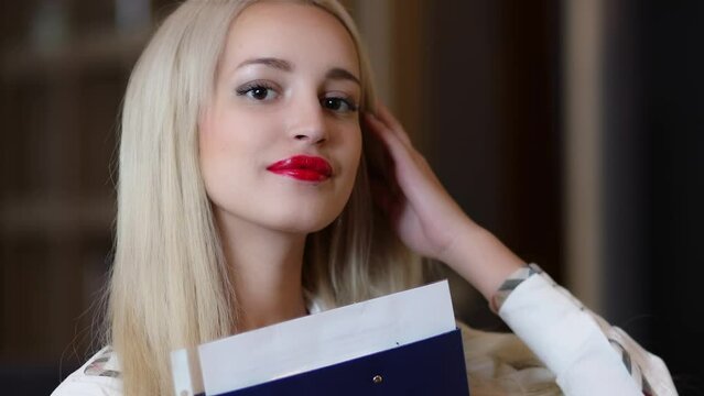 Young blonde adjusts hairs and holds paper file near face
