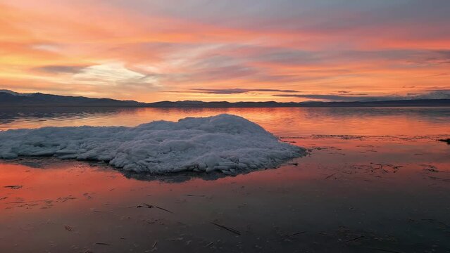 Flying slow towards ice pile on Utah Lake during colorful sunset in the winter.