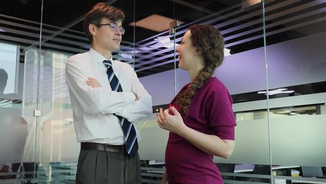 Man and woman talks and laugh among glass walls in modern office