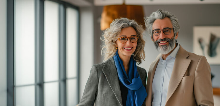 A mature, wealthy couple wearing glasses smiling in their home with copy room