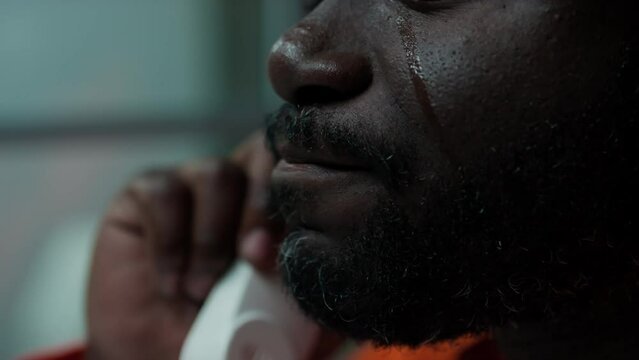 Close up shot of sad Black prisoner crying while having emotional conversation on phone in visiting room