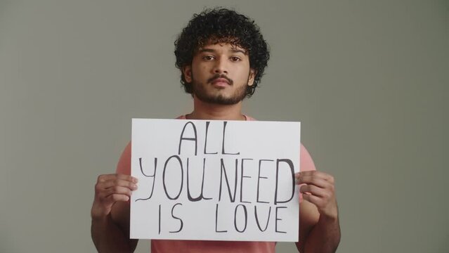 An afro american guy activist pacifist with a direct confident gaze shows poster with the slogan for love, peace, unity, equality and mutual respect between all the people in the world, denial of