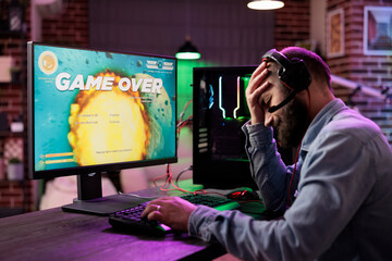 Gamer feeling depressed after losing online multiplayer action videogame match, being outsmarted by rival players. Dejected man getting headache from frustration after seeing game over screen