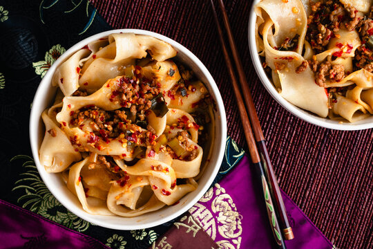 Bowls of Biang Biang Noodles Topped with Spicy Chili Oil Sauce: Biang biang mian topped with minced pork and chili oil served in bowls with chopsticks