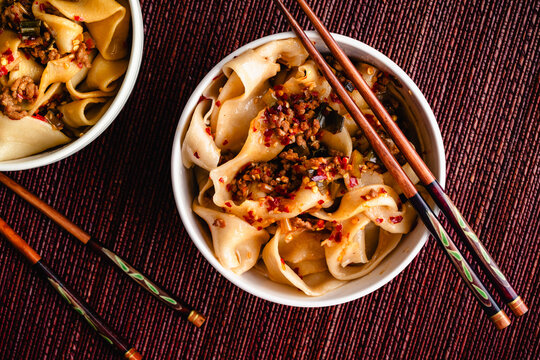 Bowls of Biang Biang Noodles Topped with Spicy Chili Oil Sauce: Biang biang mian topped with minced pork and chili oil served in bowls with chopsticks