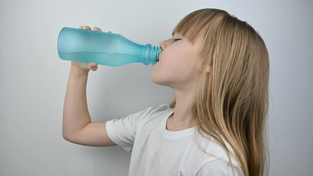 A little girl with beautiful long blonde hair drinks water from a blue reusable bottle. 