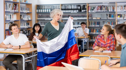 Pupils having lesson of geography. Female teacher discussing with children about national flag of Russia in college library