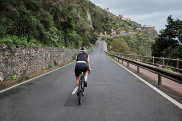 A female cyclist is riding a bicycle on an empty mountain road on Tenerife Island back view....
