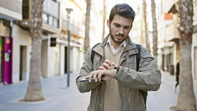 A young hispanic man with a beard uses a smartphone on a sunny urban street, depicting modern connectivity and city life.