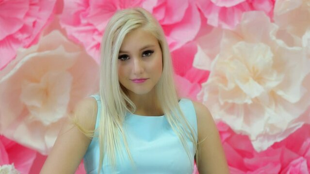Attractive blonde in cyan dress looks around near wall with flowers