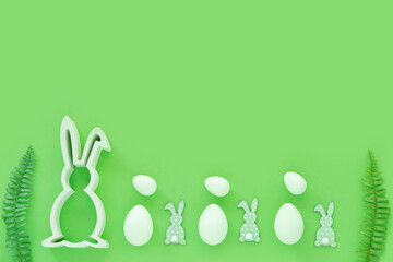 Easter eggs with wood rabbits, green leaves on green background. Egg hunting.