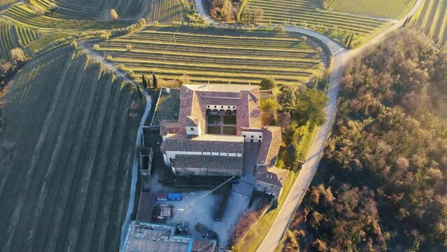 Italian vineyards with old abbey and beautiful winter colors . Aerial view of hills in the italy countryside. Bright sun light during sunset in golden hour. Autumn landscape with filds and building