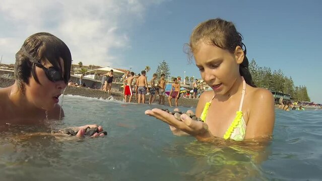 Boy and girl mr look on stones in hands in water of sea