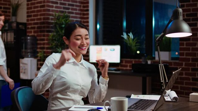 Happy office clerk celebrating finishing company project overnight by dancing on desk chair. Euphoric employee enthusiastic about finally finishing tasks on laptop, singing and jubilating