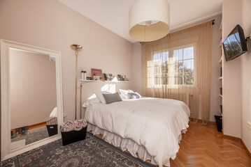A bedroom with a full length mirror with a white wooden frame and a large white down comforter