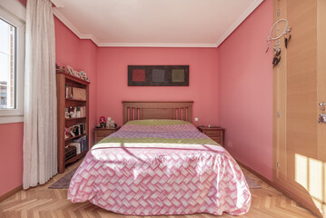 A large bedroom with a pink quilt on the bed with a wooden headboard and side tables