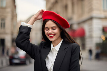 Fashion woman portrait smile with teeth standing on the street in front of the city tourist in stylish clothes with red lips and red beret, travel, cinematic color, retro vintage style, urban fashion.