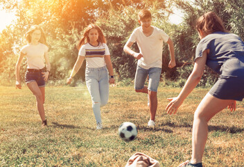 Cheerful teen friends gaily spending time together on summer day, playing with ball outdoors