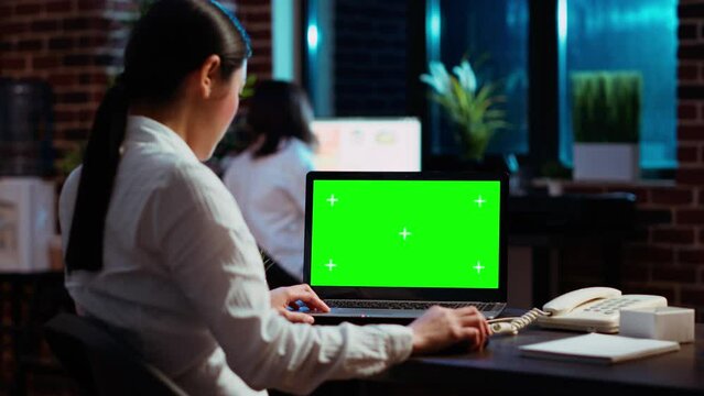 Worker looking over green screen laptop display, researching key data for company project. Businesswoman analyzing figures and charts on chroma key electronic device in office at night