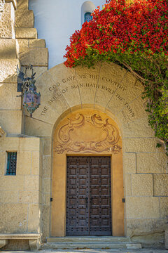 Santa Barbara, CA, USA - November 30, 2023: Santa Barbara County Courthouse monumental great arch, side door to the right with Marcus Terentius Varro inscription set in yellow stone. Red flowers