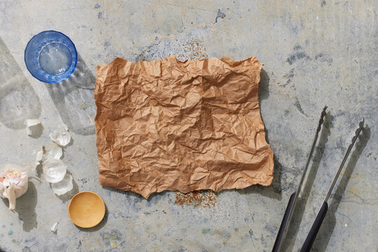 Parchement Paper on Metal Surface with Water Glass, Garlic, Spice dish, and Tongs