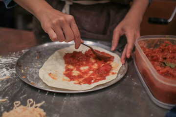 Chef hand spreading tomato sauce onto pizza. Special sauce is applied on the pizza dough and pizza ingredients
