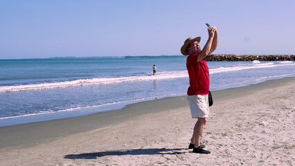 Older man wearing a vueltiao hat, red T-shirt and shorts, taking a selfie on the beautiful beaches of Cartagena de Indias, Colombia.