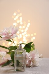 Bottle of perfume and beautiful lily flowers on table against beige background with blurred lights, space for text