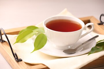 Aromatic tea in cup, saucer, spoon and green leaves on table