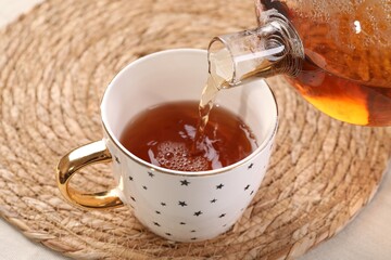 Pouring aromatic tea into cup at table, closeup
