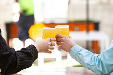 Woman and man's hands are seen clinking two glasses of beer.