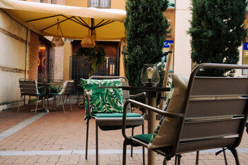 View of a cozy cafe terrace with garden furniture - tables and chairs with pillows with green tropical palm leaves. Hotel restaurant backyard.