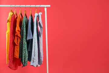 Bright clothes hanging on rack against red background, space for text. Rainbow colors