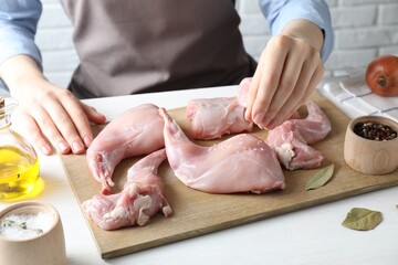 Woman putting salt onto raw rabbit meat at white wooden table, closeup