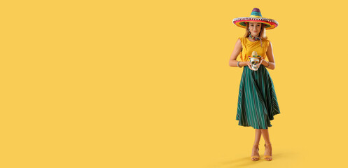 Beautiful Mexican woman in sombrero hat and with painted skull on yellow background with space for text