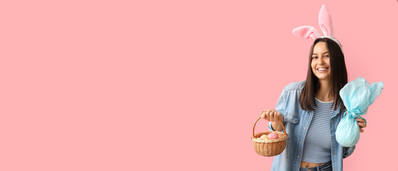 Pretty young woman with bunny ears, Easter basket and gift on pink background with space for text