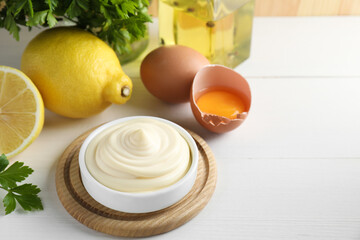 Fresh mayonnaise sauce in bowl and ingredients on white wooden table, space for text