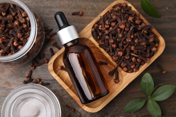 Clove oil in bottle and dried buds on wooden table, flat lay