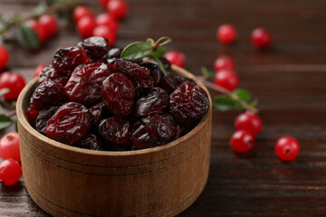 Tasty dried cranberries in bowl, fresh ones and leaves on wooden table, closeup. Space for text