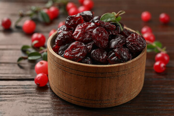 Tasty dried cranberries in bowl, fresh ones and leaves on wooden table, closeup