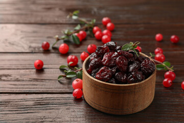 Tasty dried cranberries in bowl, fresh ones and leaves on wooden table, closeup. Space for text