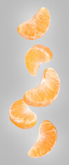 Pieces of fresh ripe tangerine falling on grey background