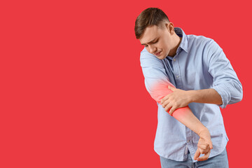 Fototapeta na wymiar Young man feeling pain in elbow on red background
